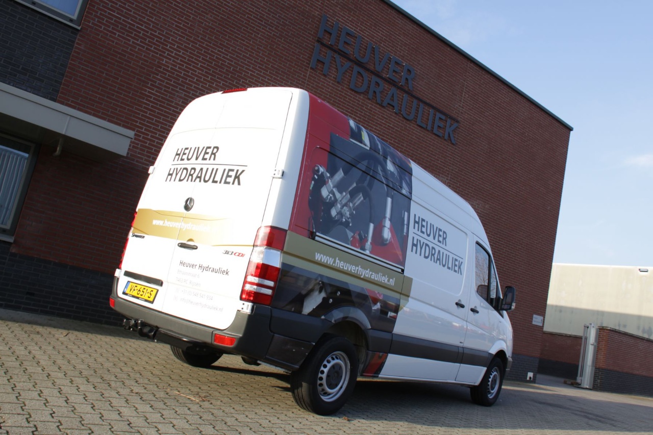 Bedrijfsbus van Heuver Hydrauliek met logo, hydrauliek onderdelen en website op bestickering geparkeerd bij bedrijfspand