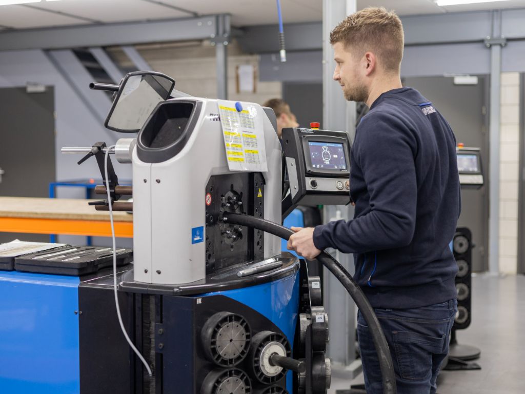 Monteur perst hydrauliekslang op maat met slangenpers in werkplaats