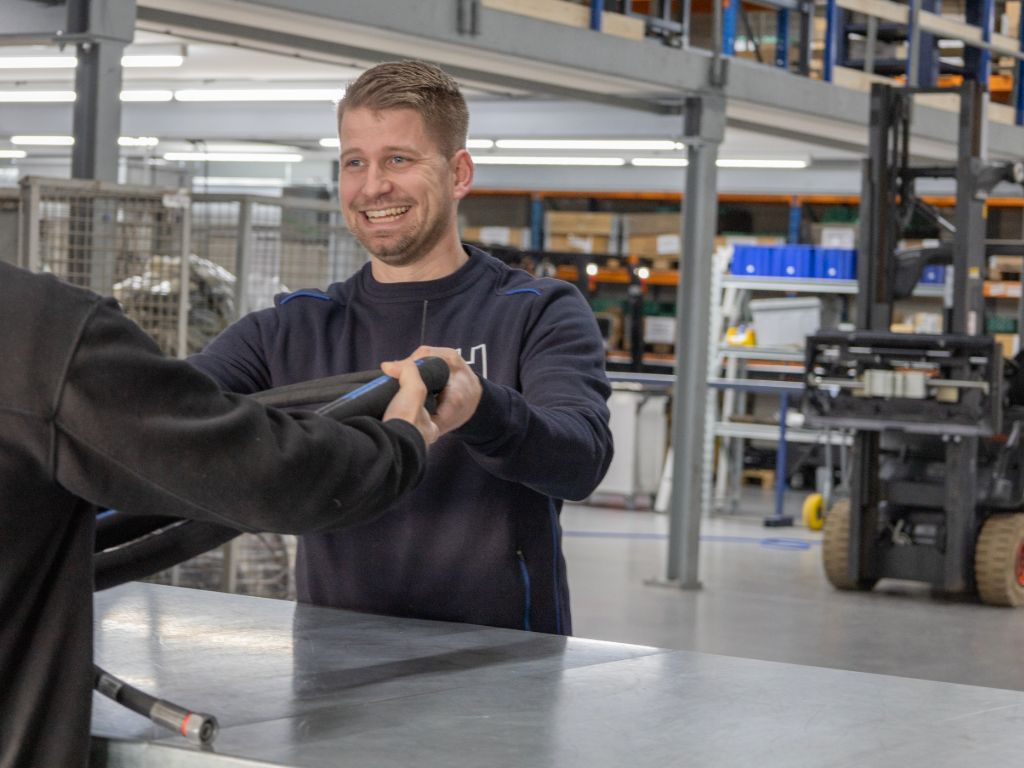 Heuver Hydrauliek medewerker overhandigt een hydraulische slang aan een klant bij de balie in het magazijn.