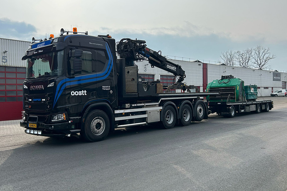 Vrachtwagen met autolaadkraan van Oostt vervoert zwaar materieel op een industrieterrein, hydraulisch ondersteund transport