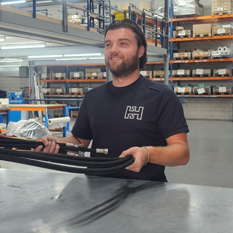 Heuver Hydrauliek medewerker houdt hydraulische slangen met koppelingen vast in het magazijn voor snelle levering.